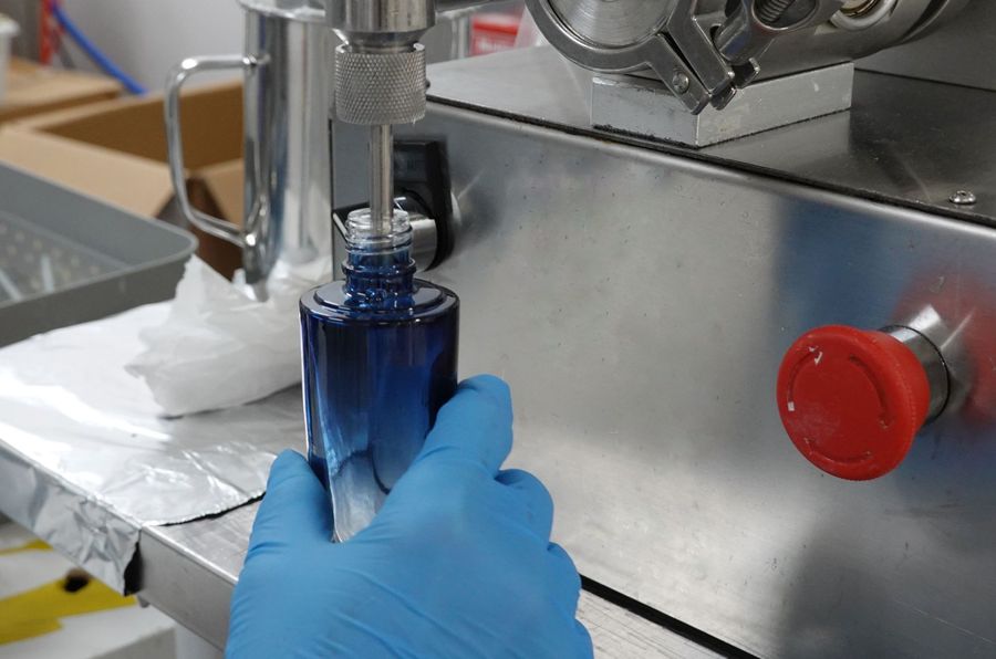 Gloved hand holding a blue glass serum bottle at the filling machine
